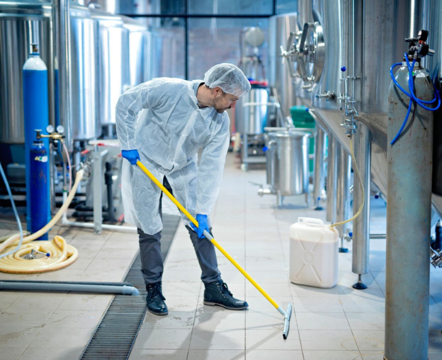 Worker cleaning the floor in a sterile production facility wearing protective gear.