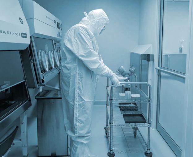 Scientist in protective gear working with equipment in a cleanroom laboratory.