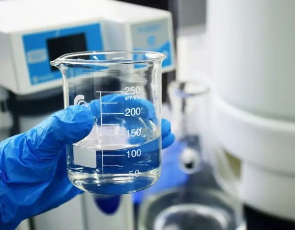 Scientist holding a beaker with water, wearing a protective glove in a laboratory.